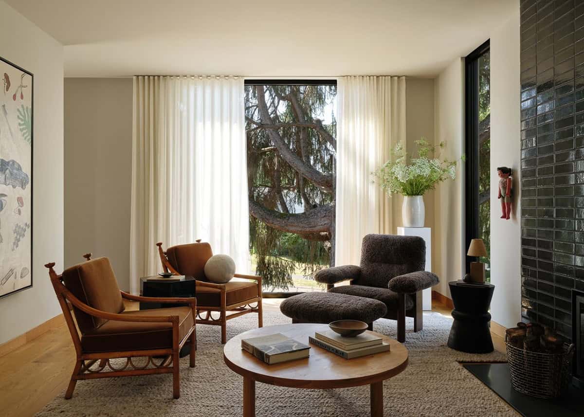 Living room with mixed vintage chairs, round coffee table, dark tiled fireplace, and floor-to-ceiling window