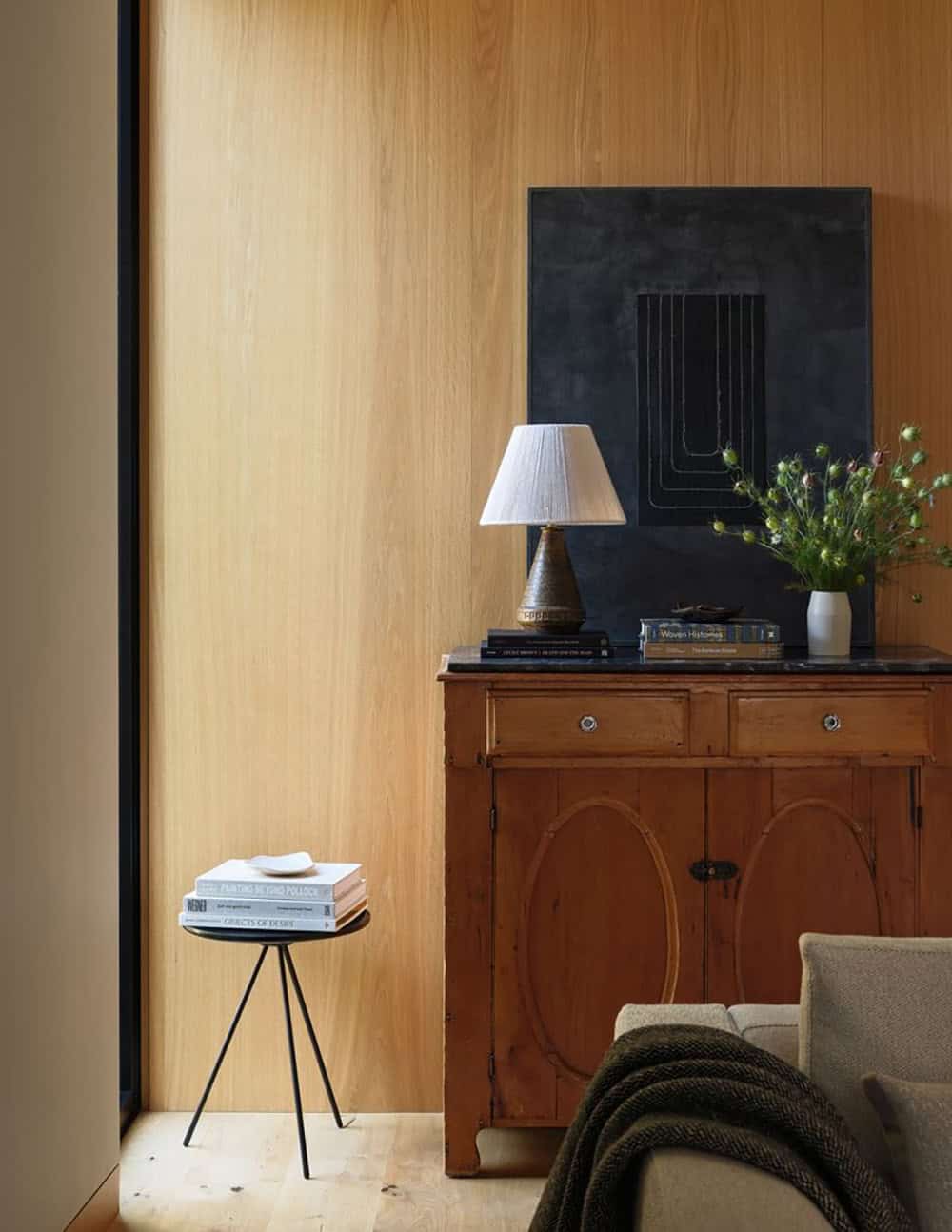 Antique pine sideboard against white oak paneling with abstract artwork and table lamp