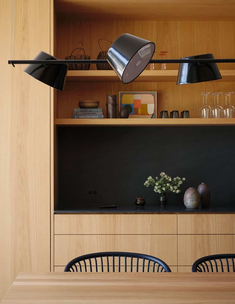 White oak built-in shelving with black pendant lamp and decorative objects above dining chairs
