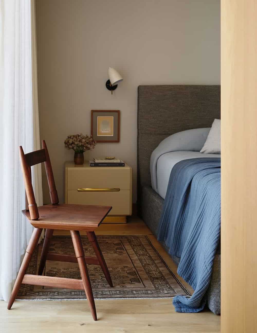Bedroom corner with walnut chair, mustard nightstand, and upholstered headboard in blue linens