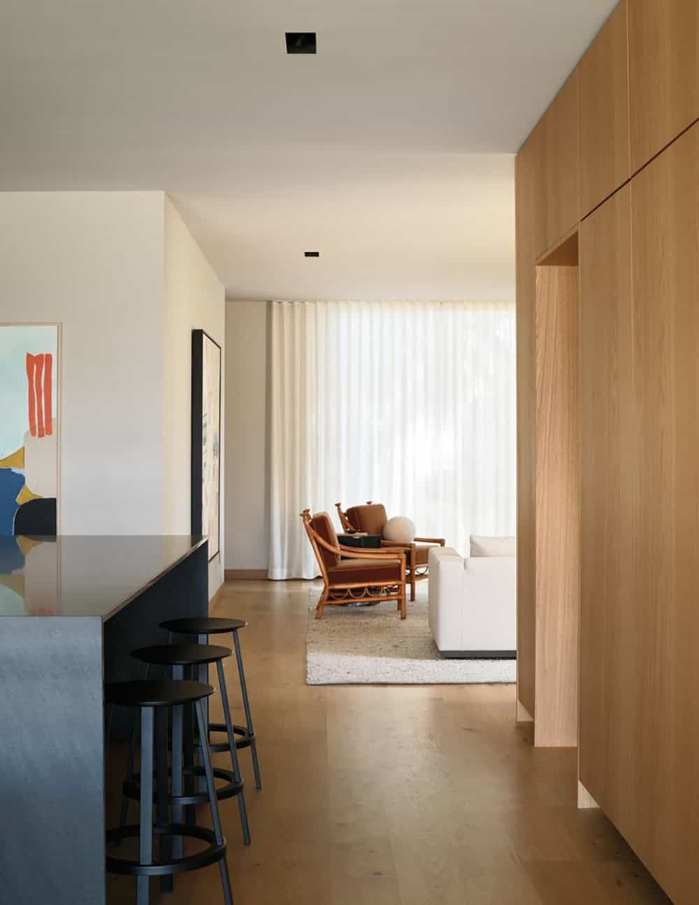 Open-plan interior view through kitchen island toward living room with sheer curtains