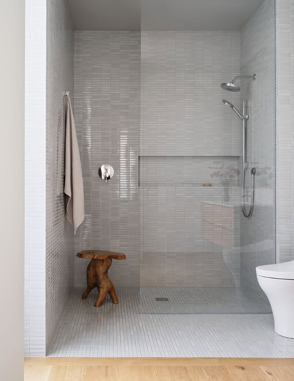 Walk-in shower with gray stacked tile, glass partition, and live-edge wood stool