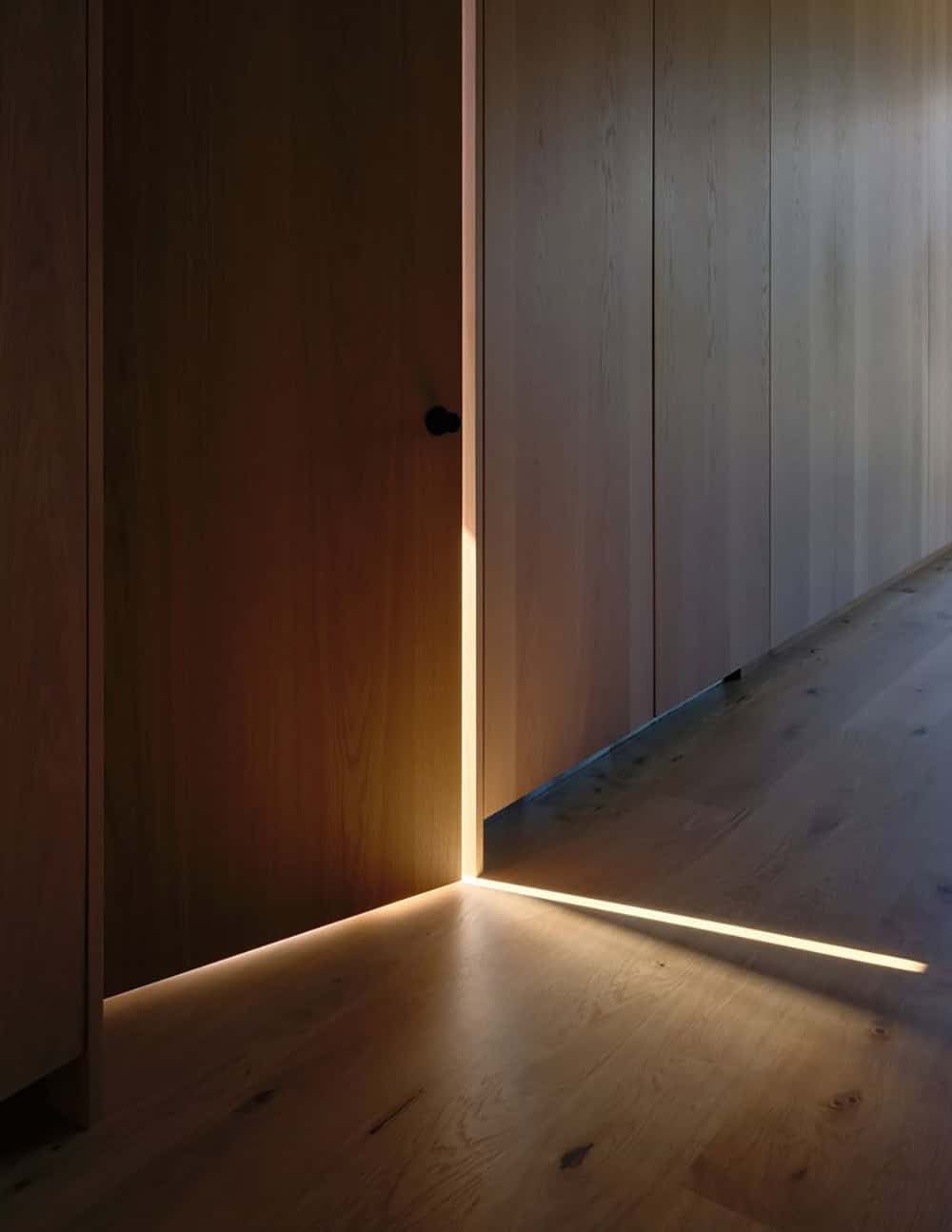 Wood-paneled hallway with warm light glowing beneath an ajar door