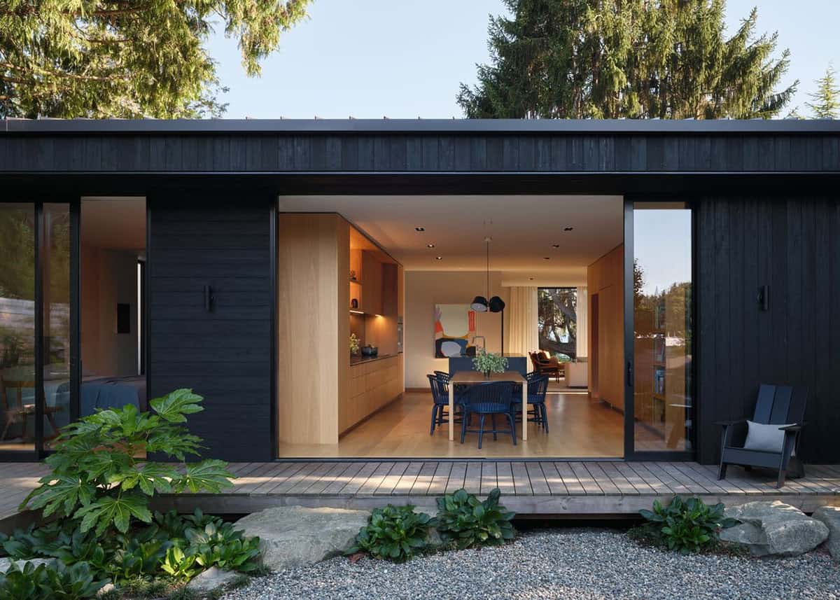 Dusk exterior view through wide open sliding doors into lit kitchen and dining room