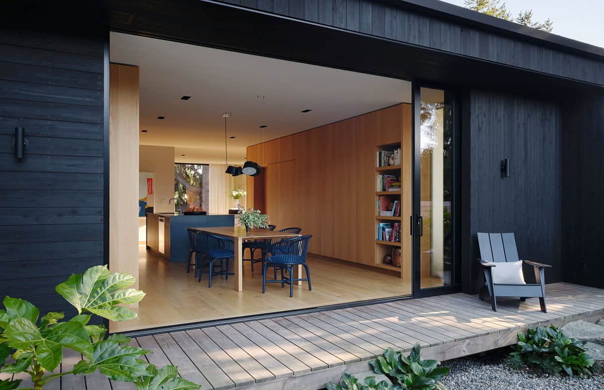 Evening exterior showing open glass wall revealing oak-clad dining and kitchen interior
