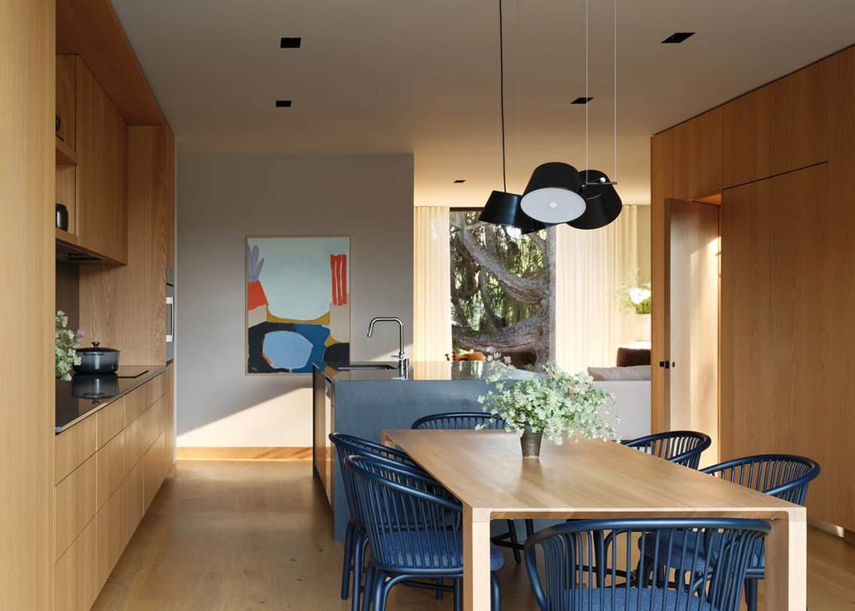 Kitchen-dining room with navy chairs, oak table, black pendants, and colorful abstract artwork