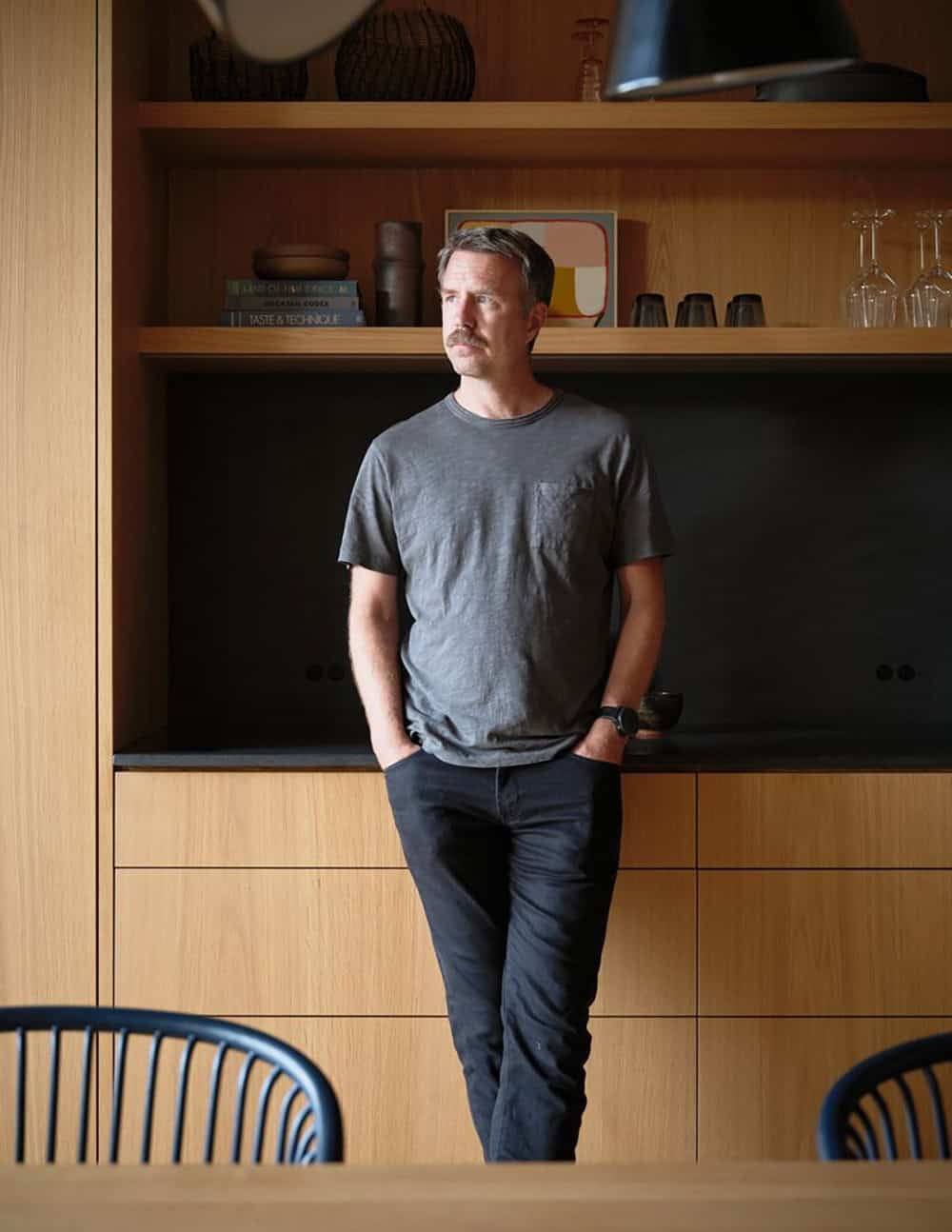 Man standing in front of white oak built-in shelving with black stone niche in kitchen dining area