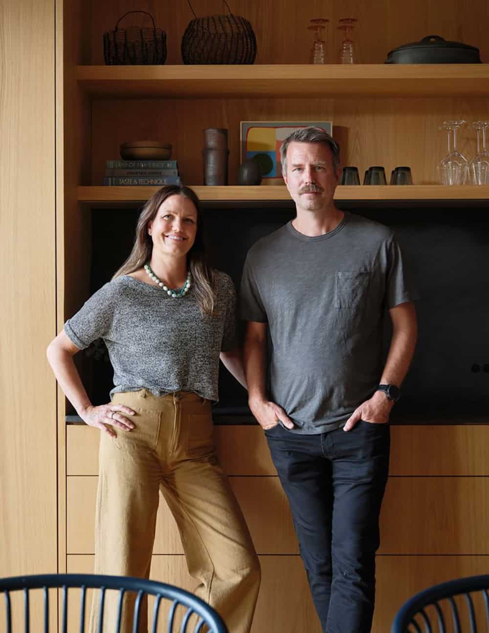 Couple standing together in front of white oak built-in shelving and black stone niche
