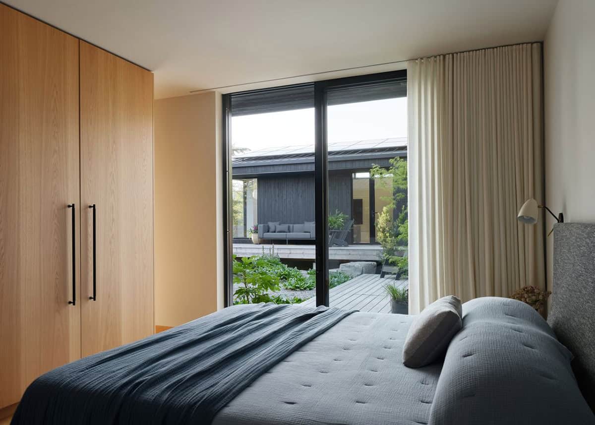 Primary bedroom with blue linen bedding, oak wardrobe, and floor-to-ceiling window overlooking garden courtyard