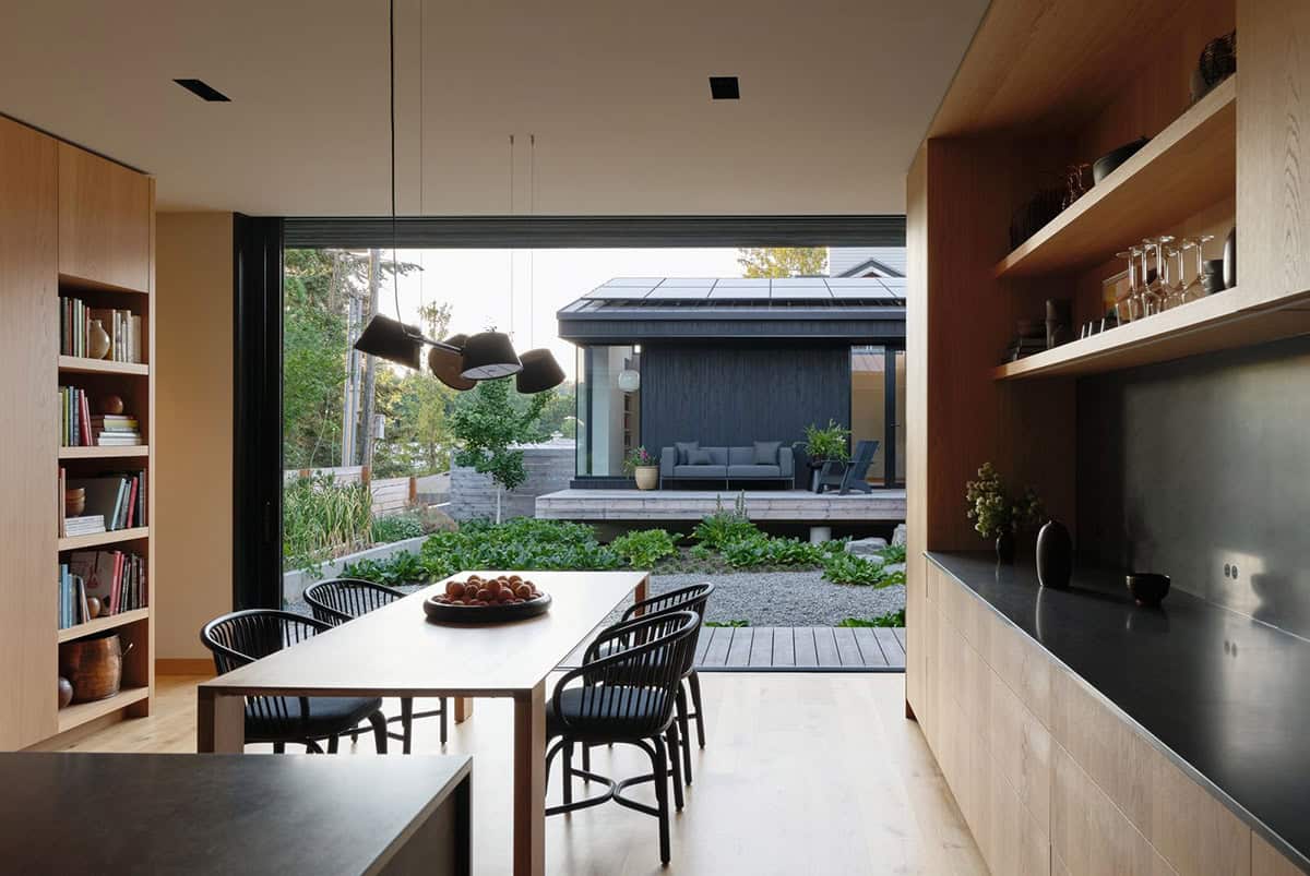 Dining room opening via large sliding glass wall to garden courtyard and dark-clad studio beyond