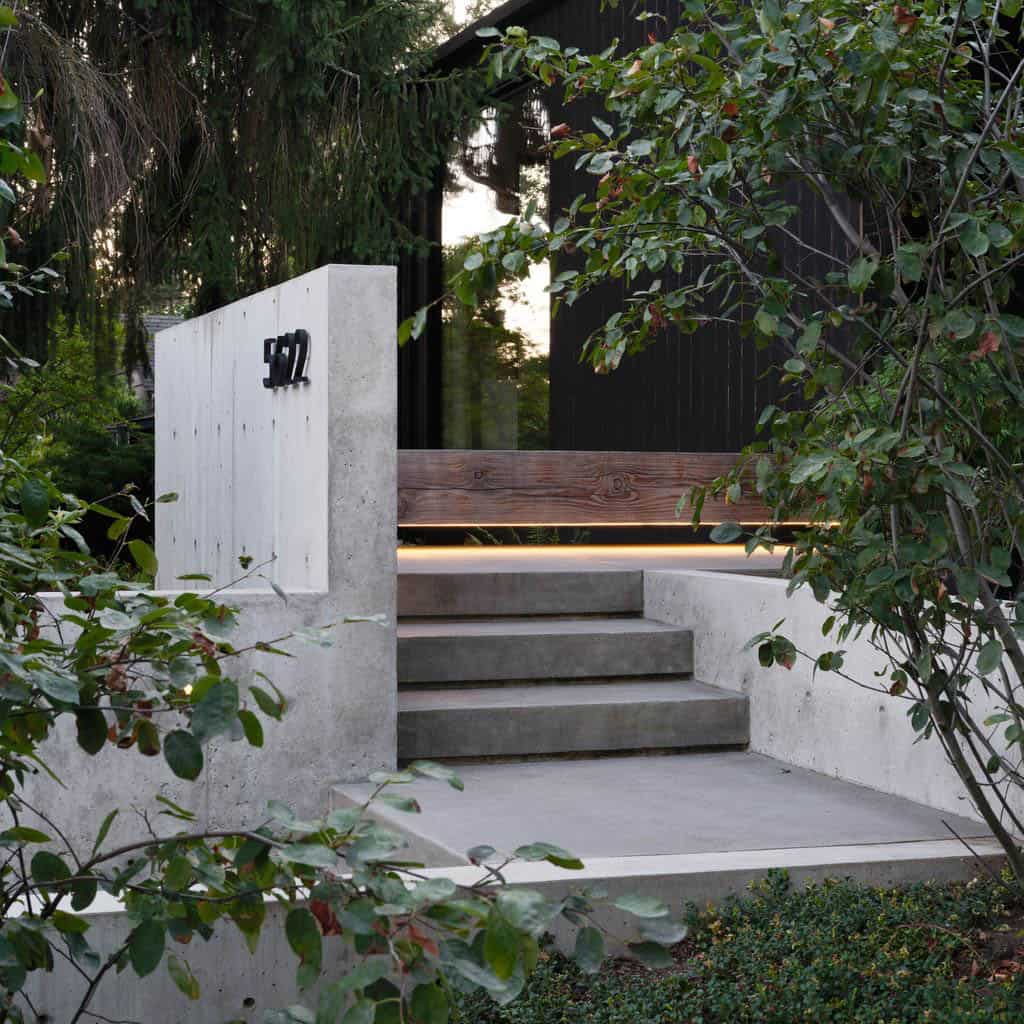 Concrete entry steps with house number plaque, wood bench detail, and lit underside at dusk