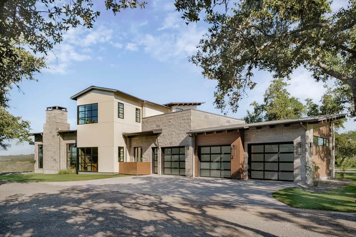 Front elevation of modern Hill Country ranch home with limestone exterior and glass garage doors