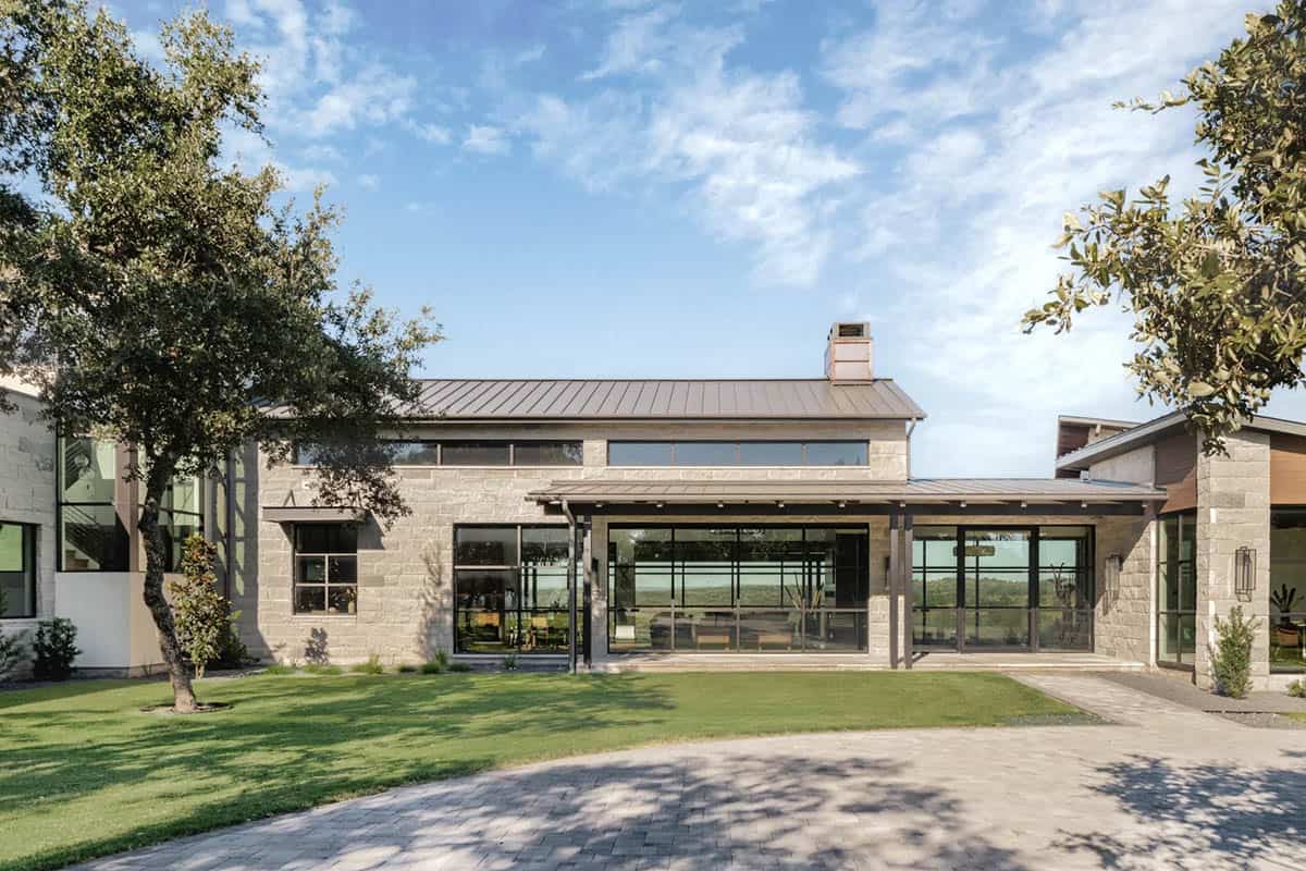 Daytime exterior of limestone ranch home with floor-to-ceiling steel windows and Hill Country views