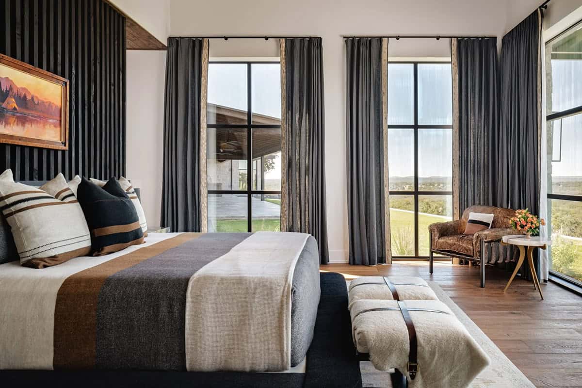 Primary bedroom with dark curtains, striped pillows and sweeping Hill Country views