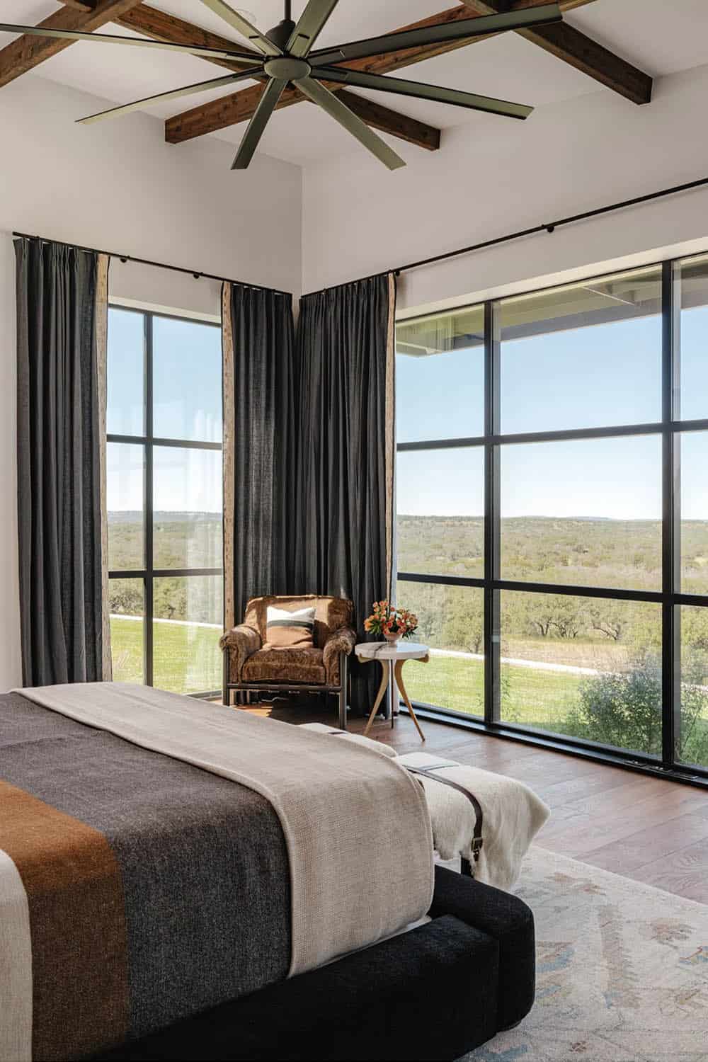 Primary bedroom corner with exposed wood ceiling beams, oversized fan and panoramic windows
