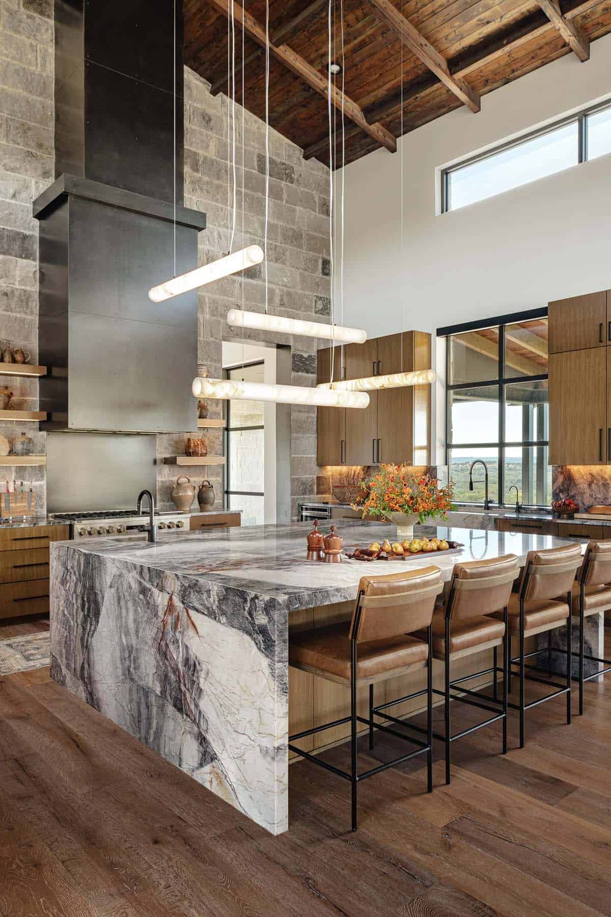 Kitchen with soaring ceilings, reclaimed wood beams, dramatic stone range wall and waterfall marble island