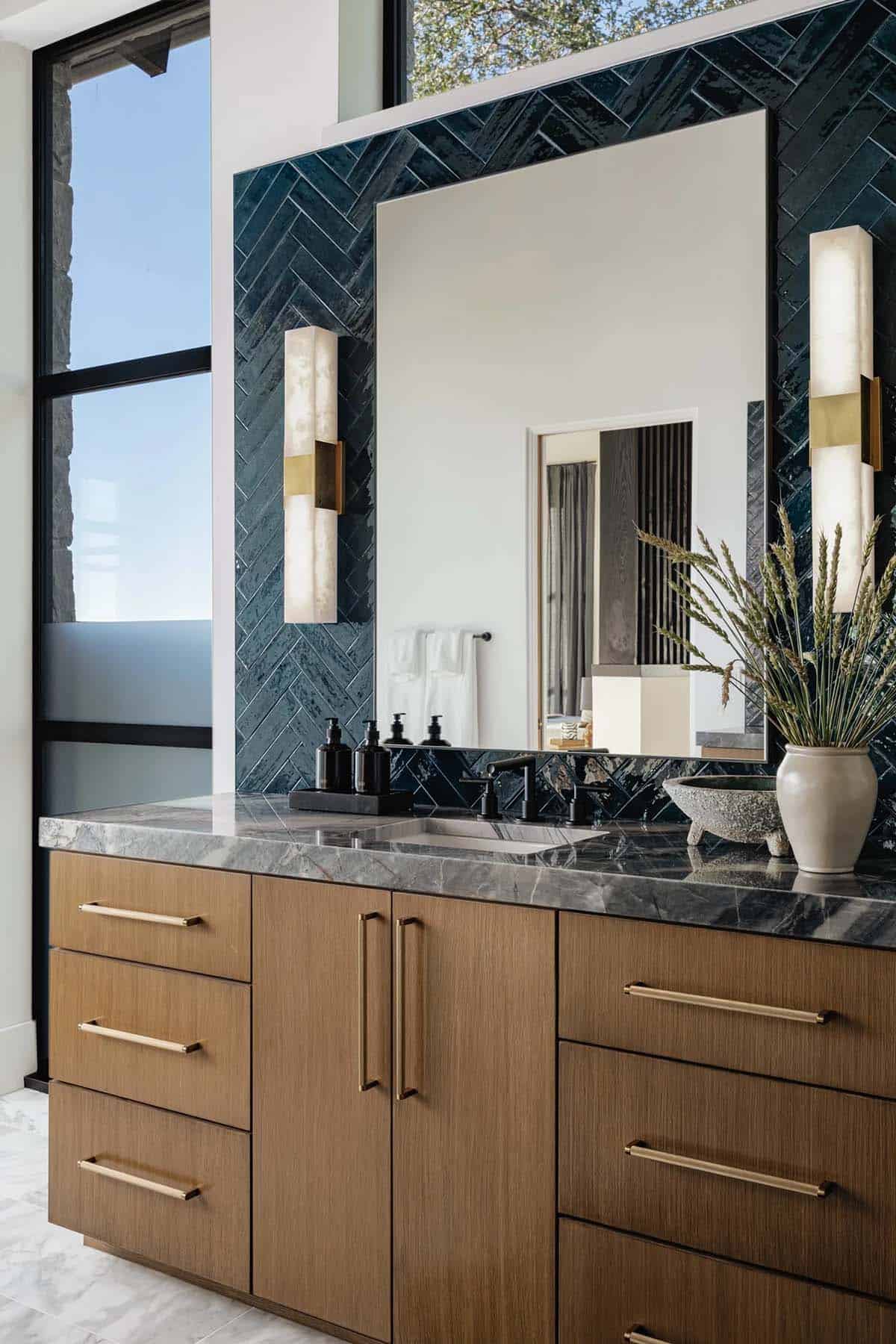 Primary bathroom vanity with teal herringbone tile, oak cabinetry and alabaster sconces