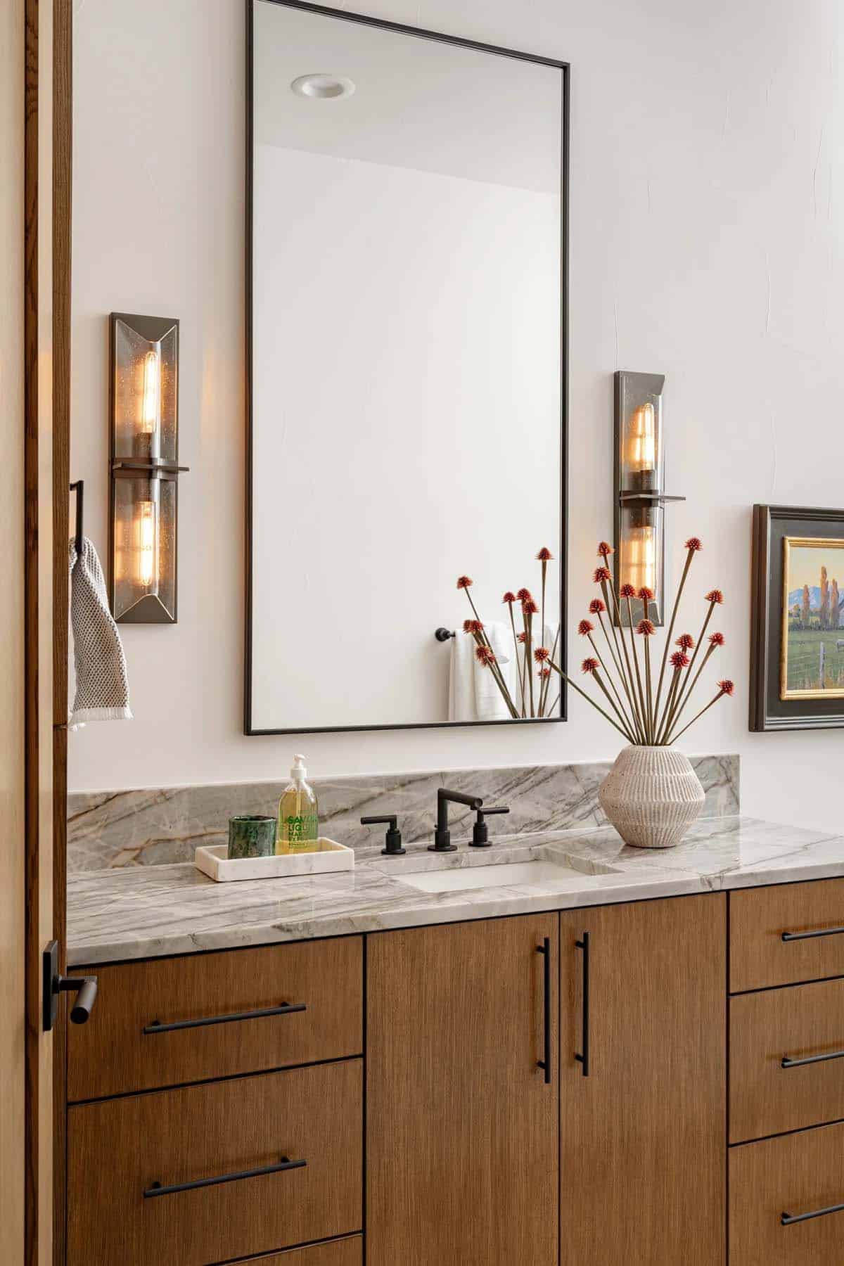 Guest bathroom vanity with marble countertop, oak cabinetry and industrial wall sconces