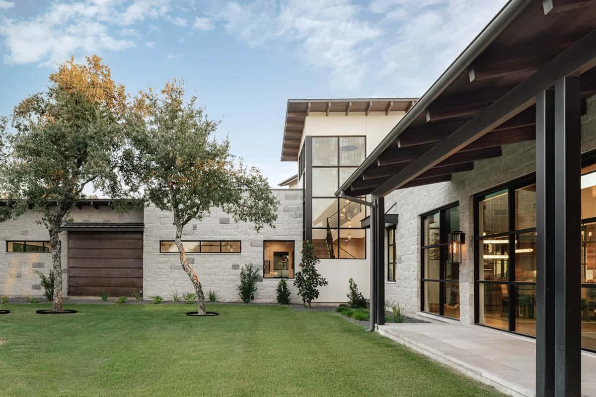 Courtyard view of limestone ranch home with covered porch and wood beam ceiling at twilight