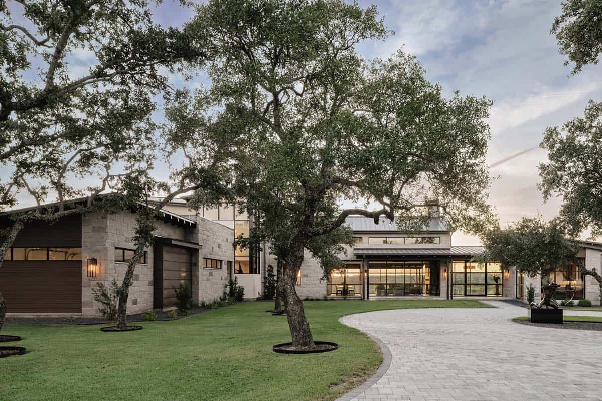Wide angle dusk view of Hill Country ranch home with circular driveway and mature live oaks