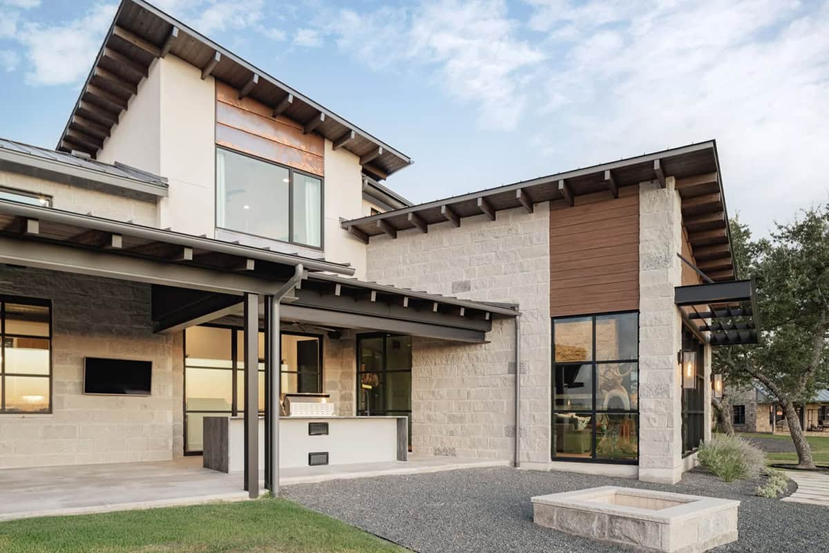 Back exterior of contemporary ranch home with limestone walls, wood siding accents and fire pit