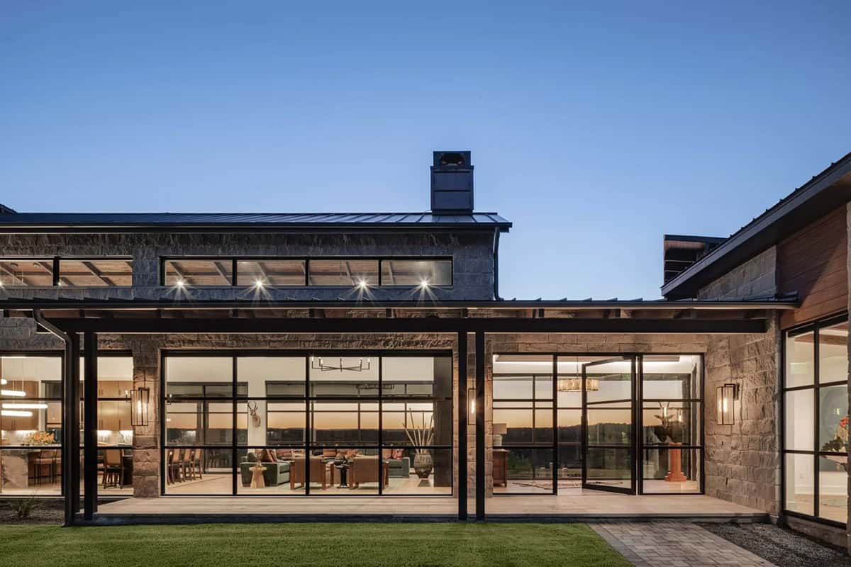 Night view of ranch home rear exterior with open steel frame windows and interior lighting
