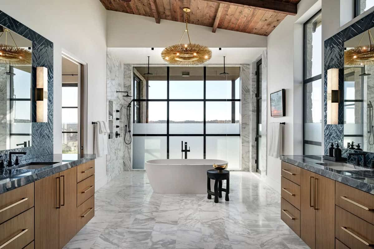 Luxurious primary bathroom with freestanding soaking tub, marble floors, dual vanities and gold chandelier