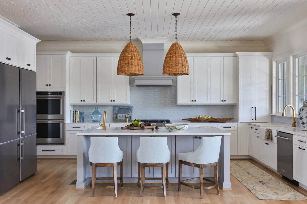 White kitchen with wicker pendant lights, gray island, upholstered barstools, light blue subway tile backsplash, and wood floors