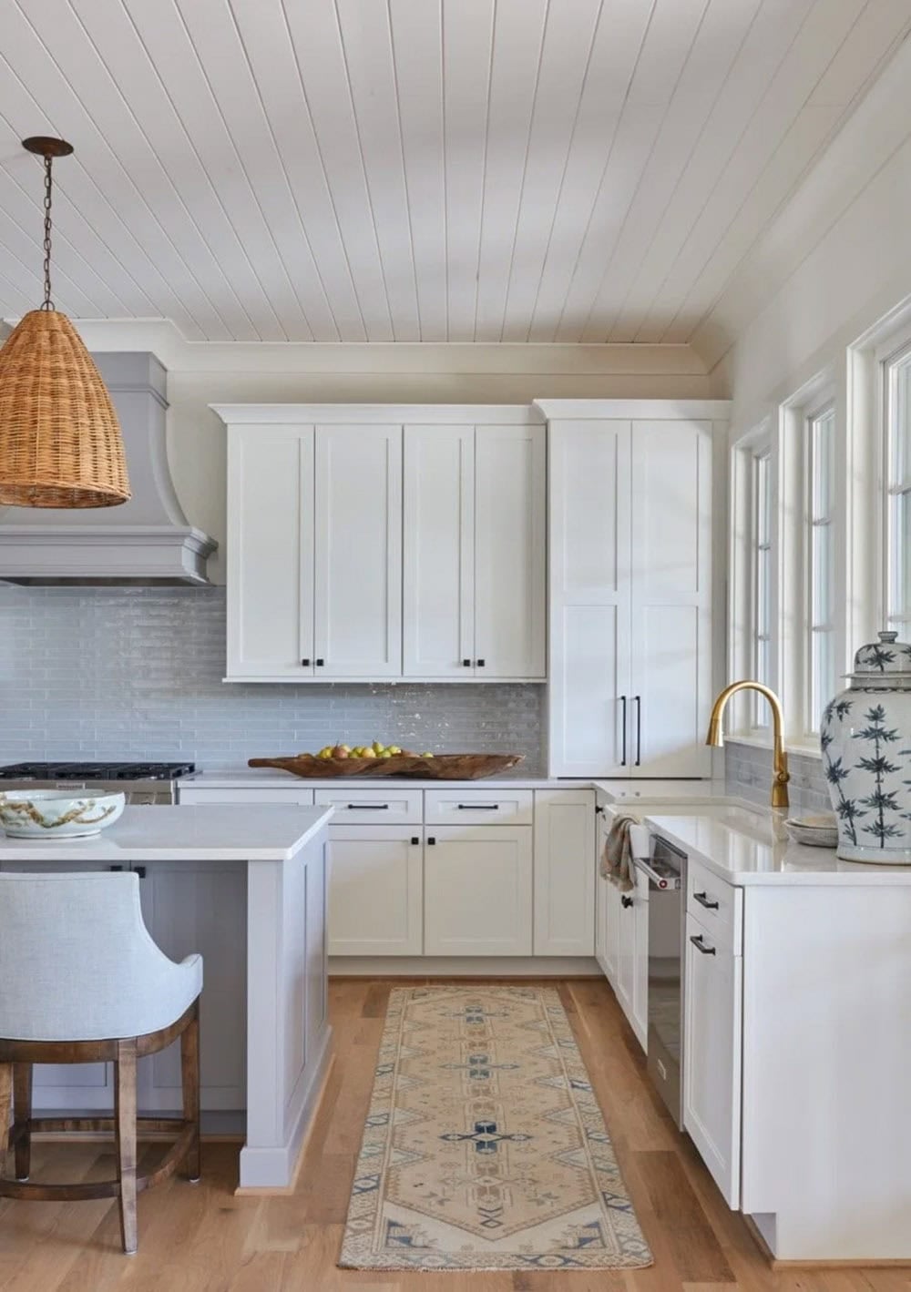 White kitchen detail with wicker pendant, blue subway tile backsplash, gold faucet, and vintage runner rug