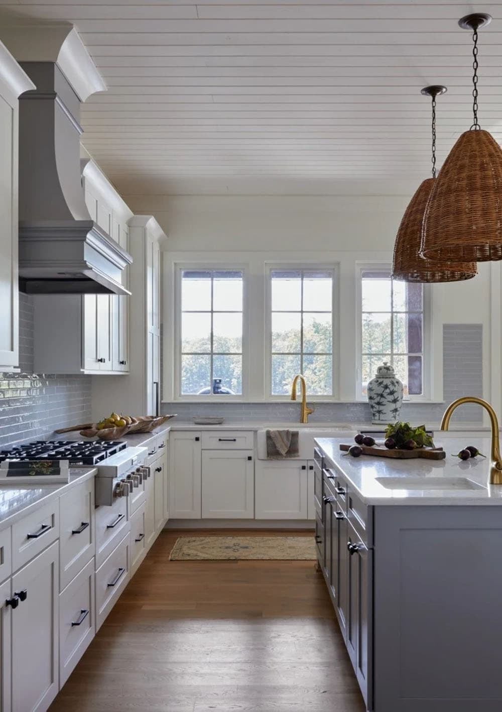 Kitchen view showing gray island with prep sink, gold faucet, professional range, and wicker pendants above
