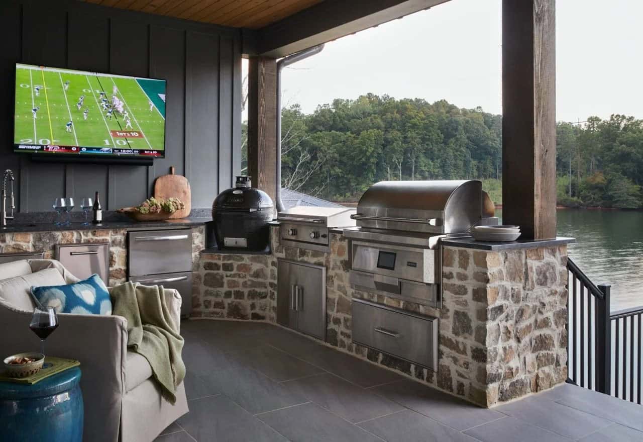 Outdoor kitchen with stone base, professional grill, kamado smoker, lake views, and wall-mounted TV