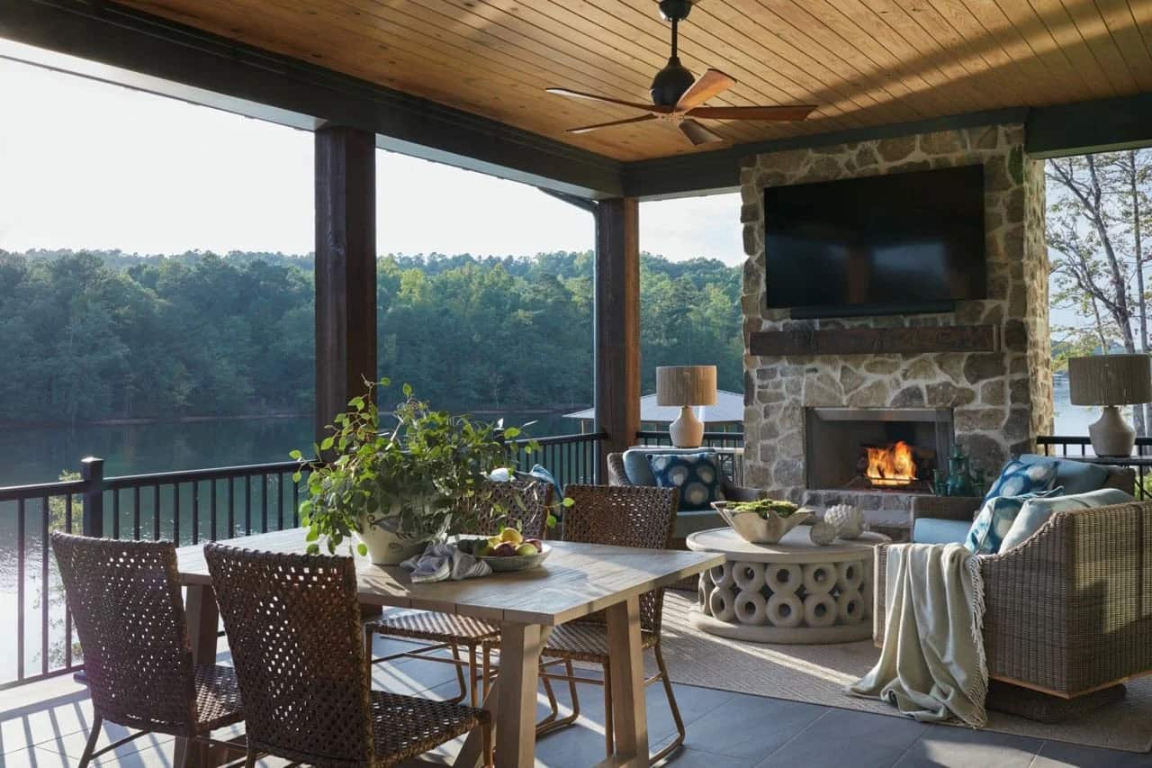 Screened porch with wicker dining and lounge seating, stone fireplace, ceiling fan, and panoramic lake views