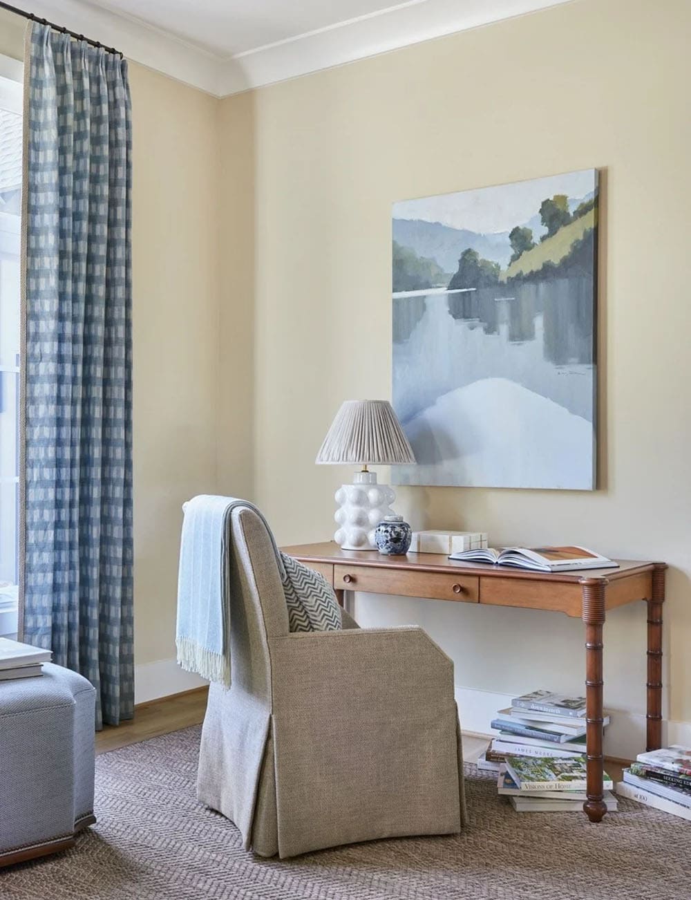 Guest bedroom sitting area with warm cream walls, blue plaid curtains, cherry wood desk, and lake landscape painting