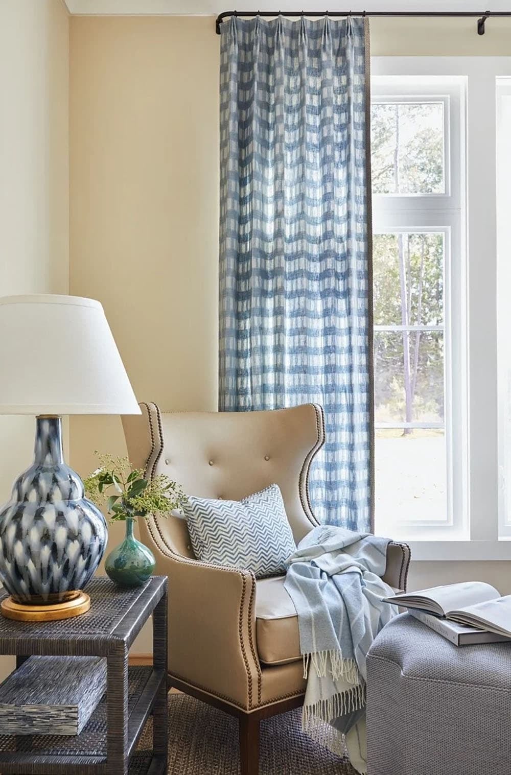 Reading nook with leather wingback chair, blue ikat plaid curtains, and blue-and-white ceramic lamp