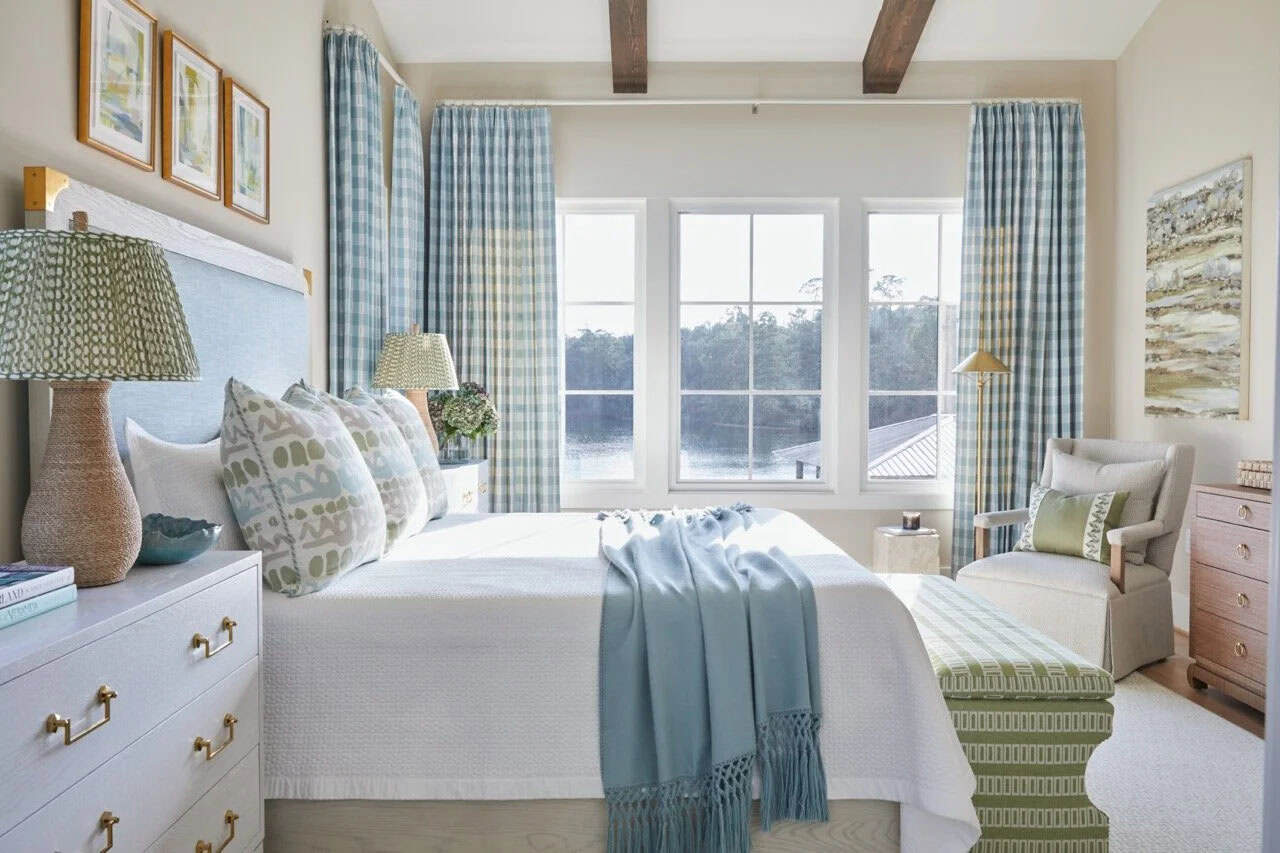 Primary bedroom with light blue upholstered headboard, plaid curtains, lake views, and green bench at foot of bed
