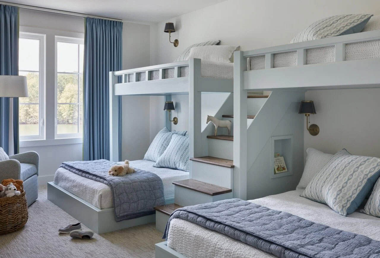 Children's bunk room with four built-in pale blue bunks, wood stair steps, brass sconce lighting, blue curtains, and lake views