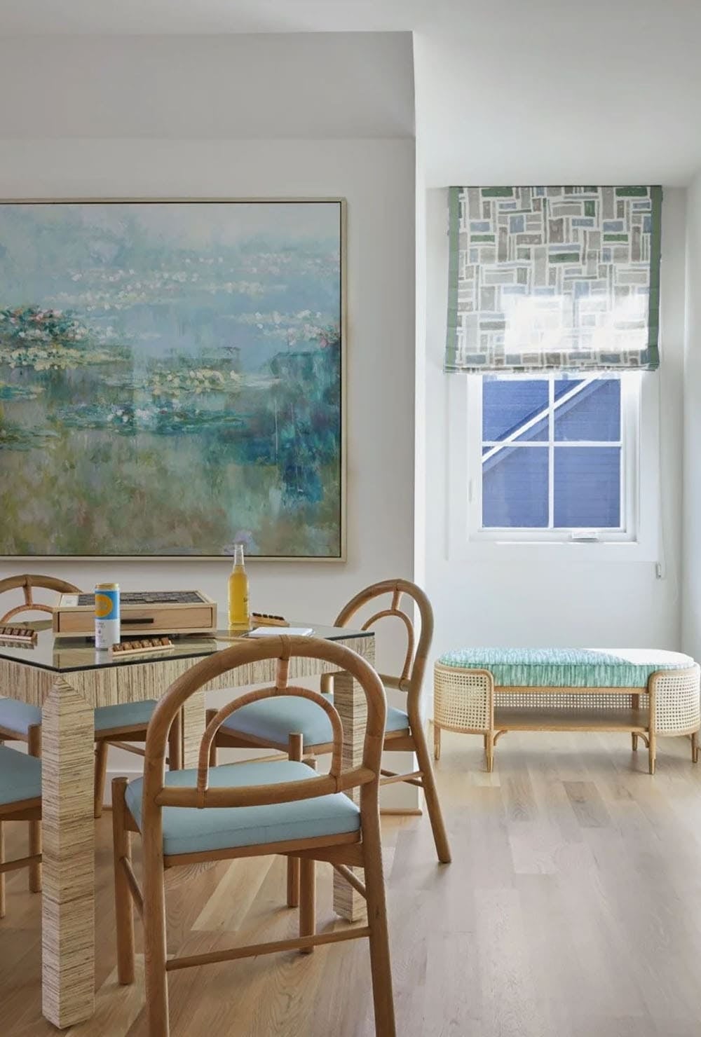Game room with rattan chairs, blue seat cushions, grasscloth-wrapped table, large impressionist water lily painting, and woven bench by window