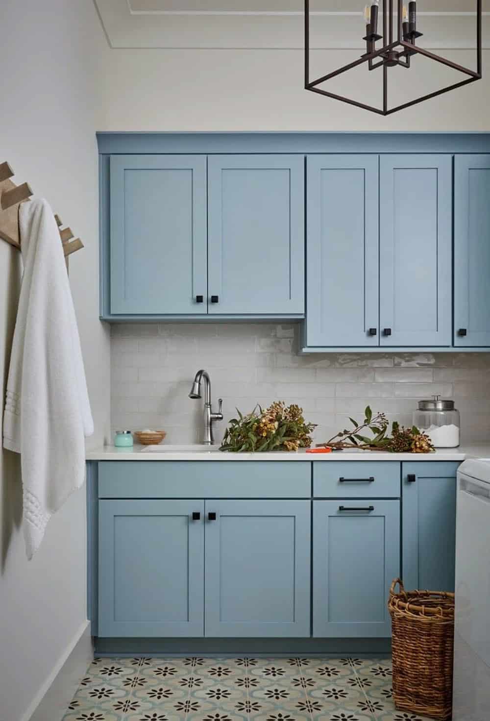 Laundry room with powder blue shaker cabinets, black hardware, patterned tile floor, white subway tile backsplash, and iron cage pendant