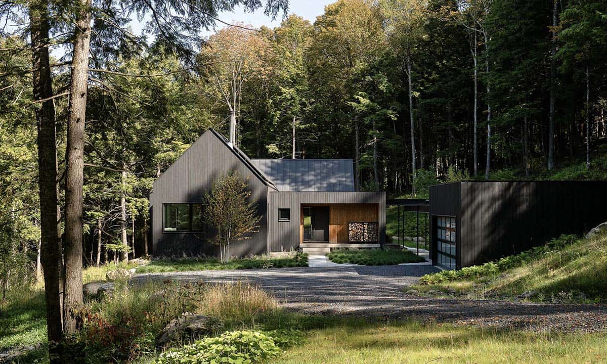Full exterior view of a dark-clad contemporary Vermont home with gabled roofline surrounded by dense woodland