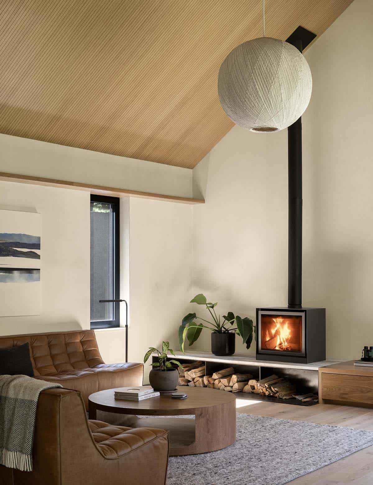 Cozy living room with vaulted wood-clad ceiling, freestanding wood-burning stove, leather chairs, and globe pendant light