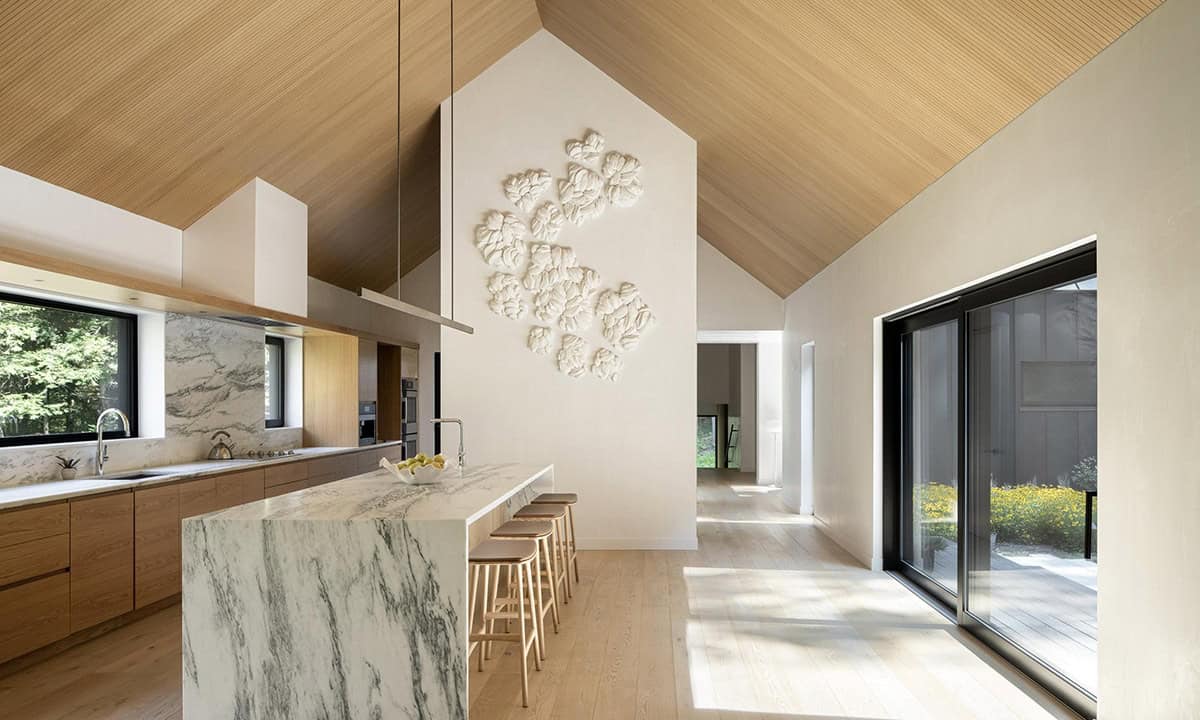 Bright kitchen with cathedral ceiling, marble island, oak cabinetry, and a large white sculptural wall installation