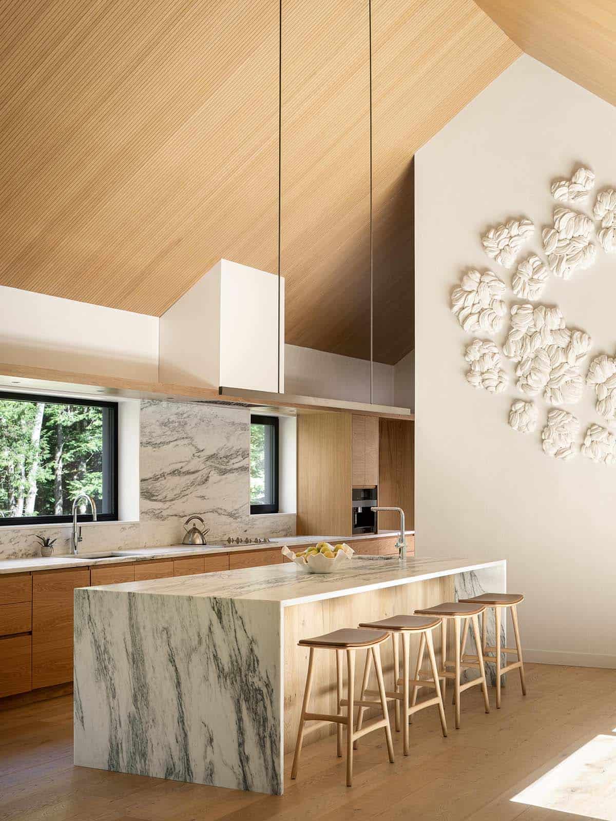 Kitchen island clad in dramatic veined marble beneath a soaring wood-paneled cathedral ceiling with sculptural wall art