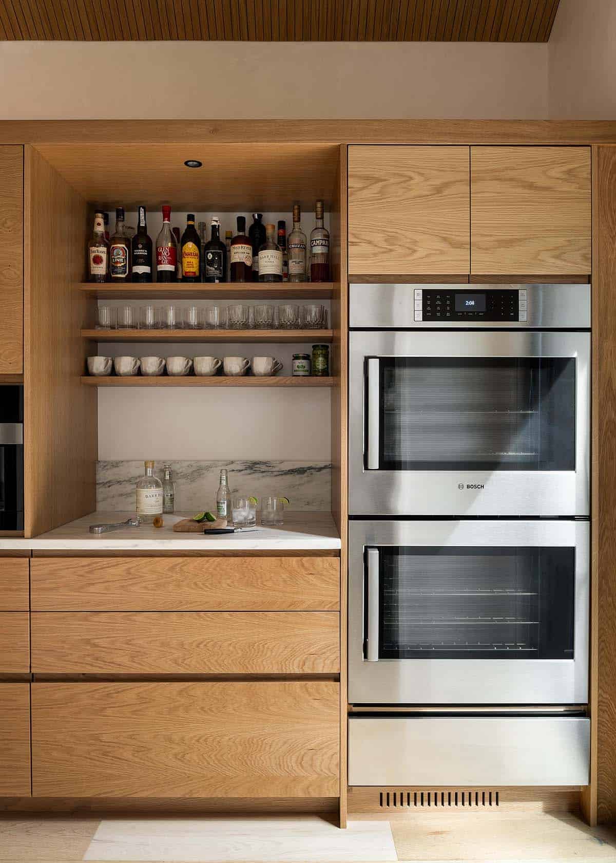 Built-in oak bar niche with open shelving and a stainless Bosch double wall oven beside it
