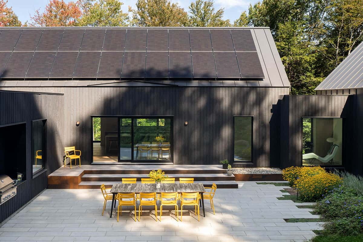 Back patio with yellow metal dining chairs, solar-paneled roof, and sliding glass doors to the interior