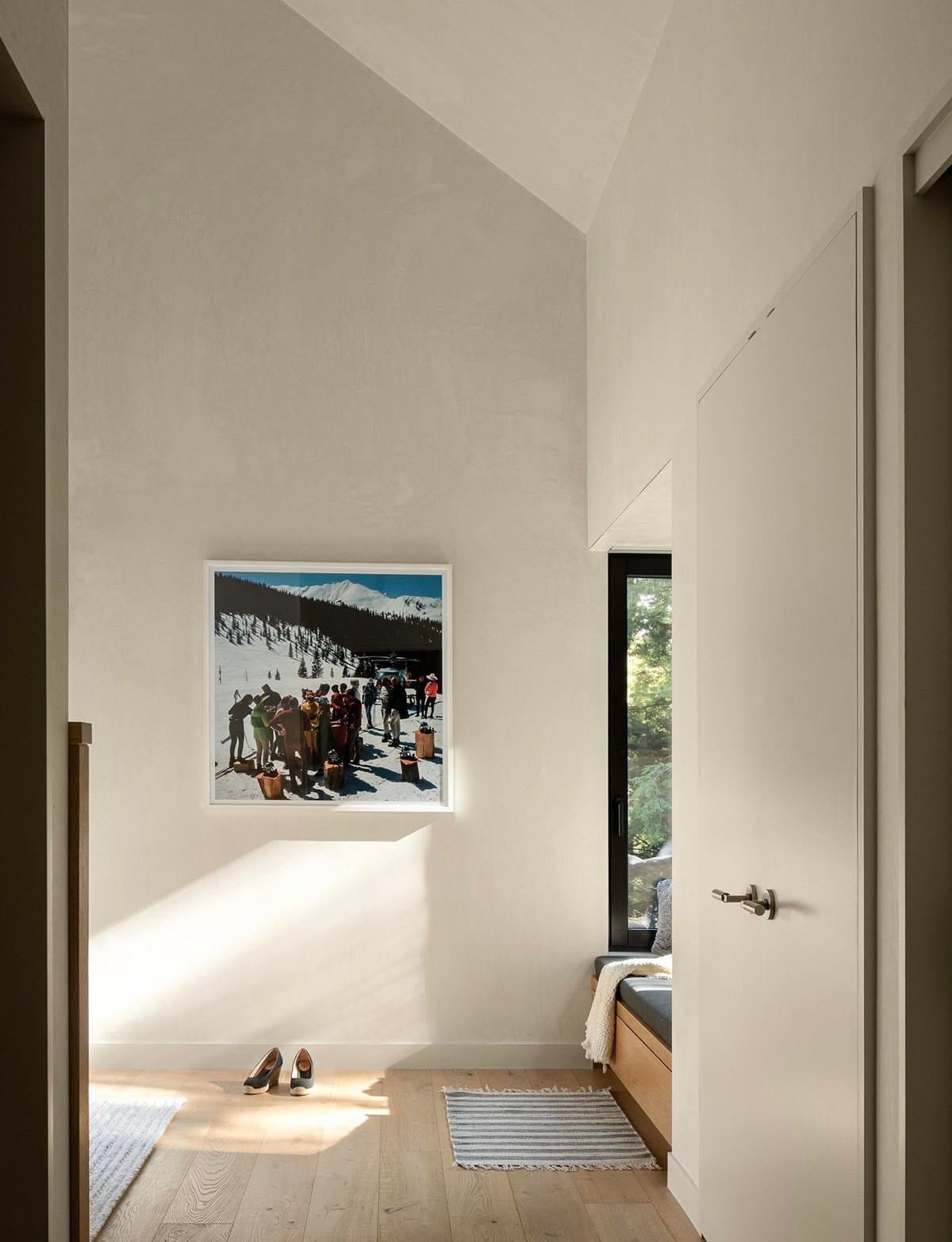 Bright hallway with high vaulted ceiling, framed ski photography, and a glimpse of a built-in window seat