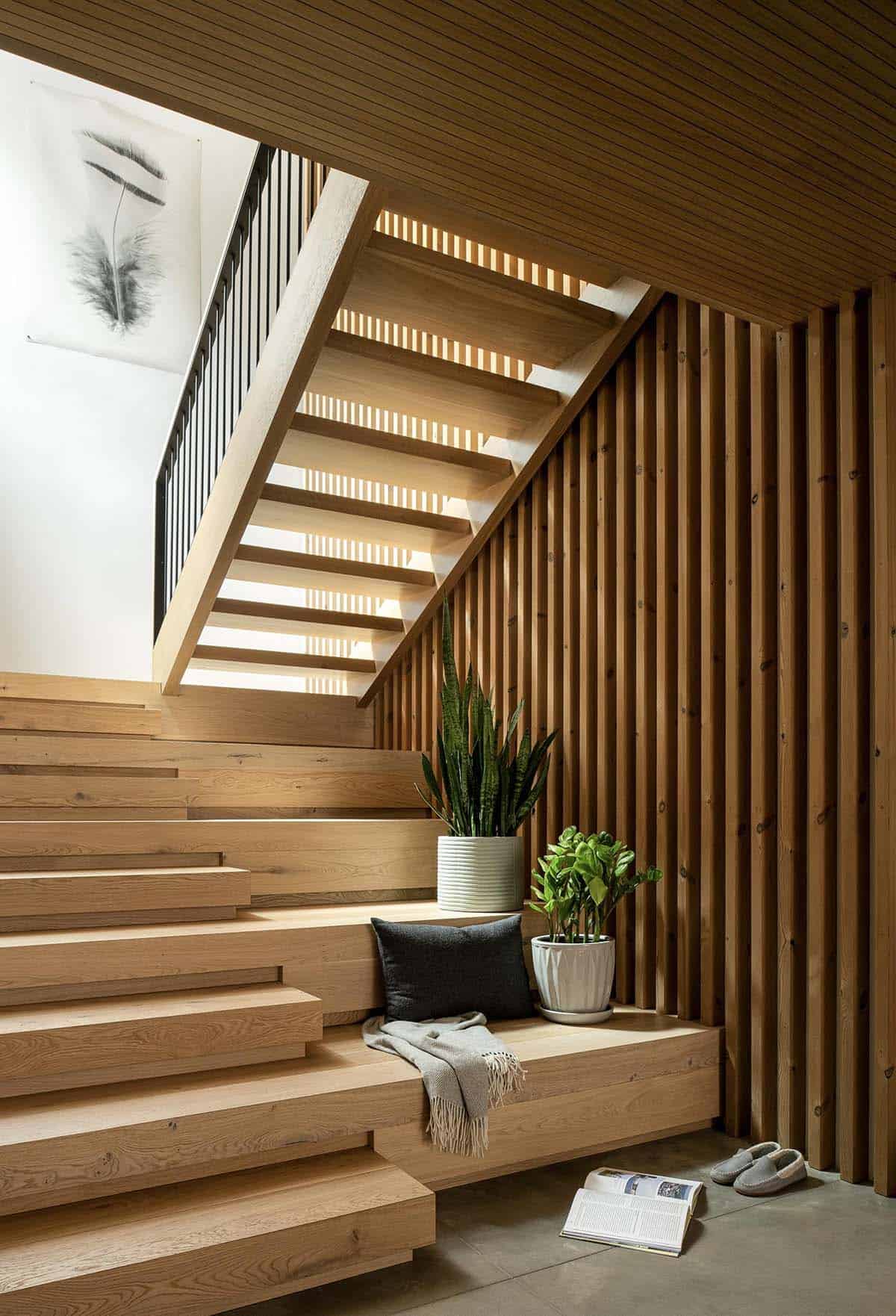 Open-tread oak staircase with vertical wood slat wall, built-in bench, and potted plants beneath a skylit landing