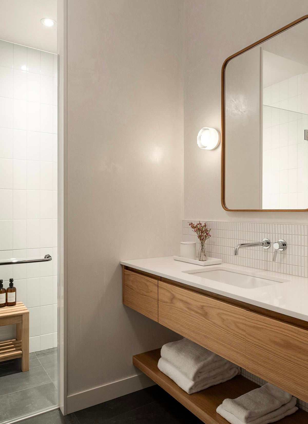 Bright bathroom with floating oak vanity, white subway tile backsplash, rounded mirror with oak frame, and glass shower enclosure