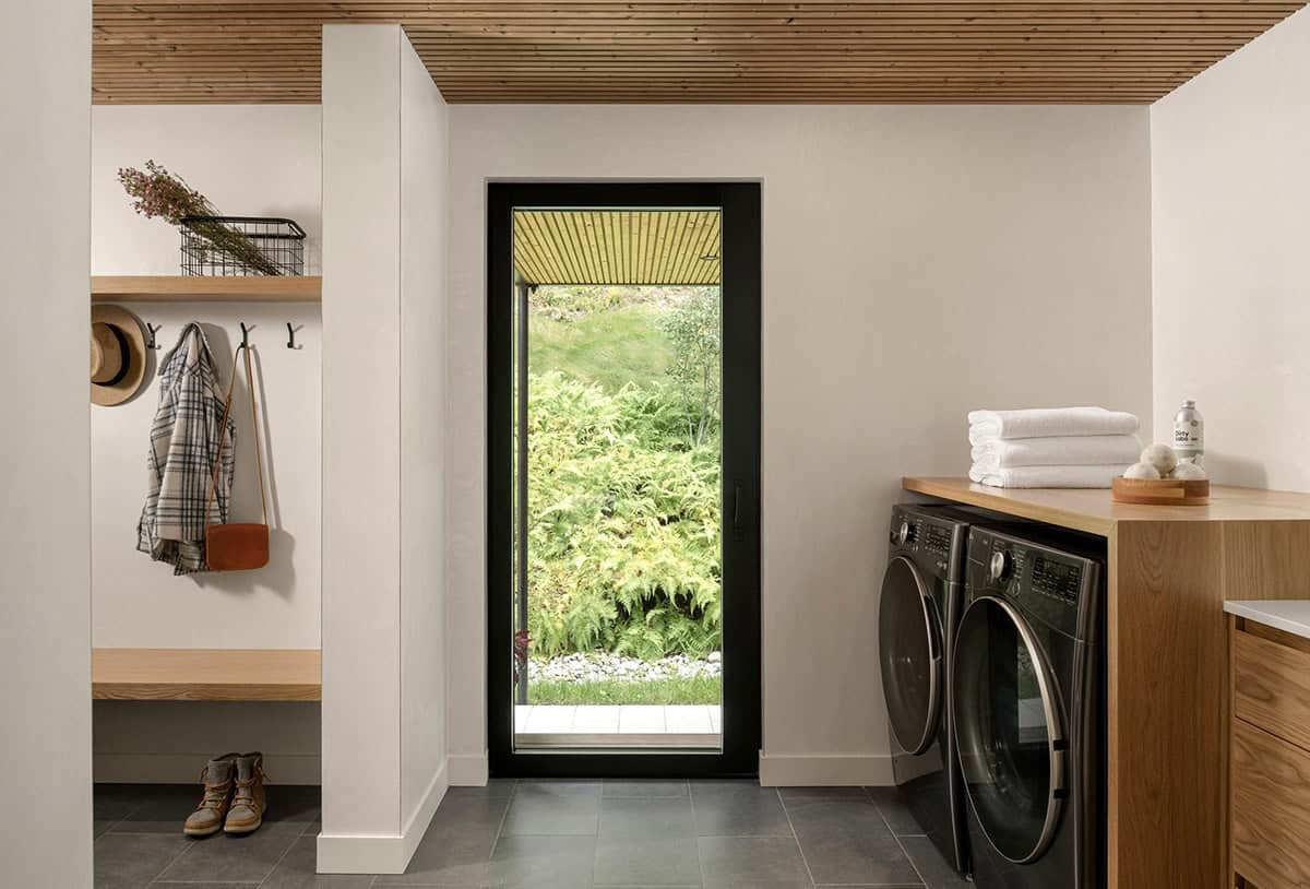Mudroom and laundry area with hook wall, open shelving, washer and dryer, and a tall black-framed garden-view window