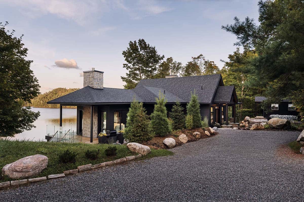 Black cottage exterior with lakeside setting, stone chimneys, and gravel driveway