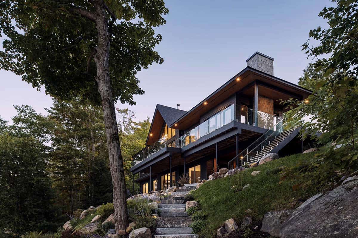 Hillside cottage at dusk with glass balcony, wooden soffits, and stone staircase through trees